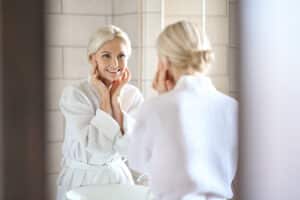 Mature woman checking her new youthful skin in the mirror after full recovery from a facelift
